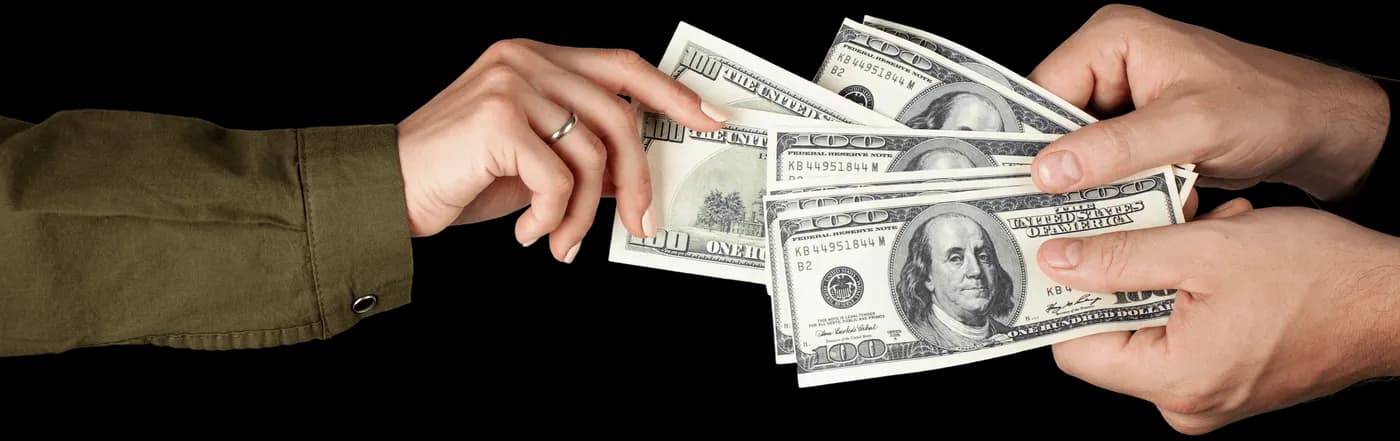 Ruce si předávají americké dolarové bankovky